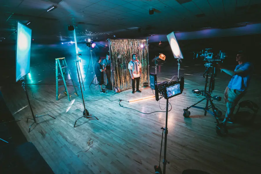 A lit studio set with a presenter, lights, and a camera crew